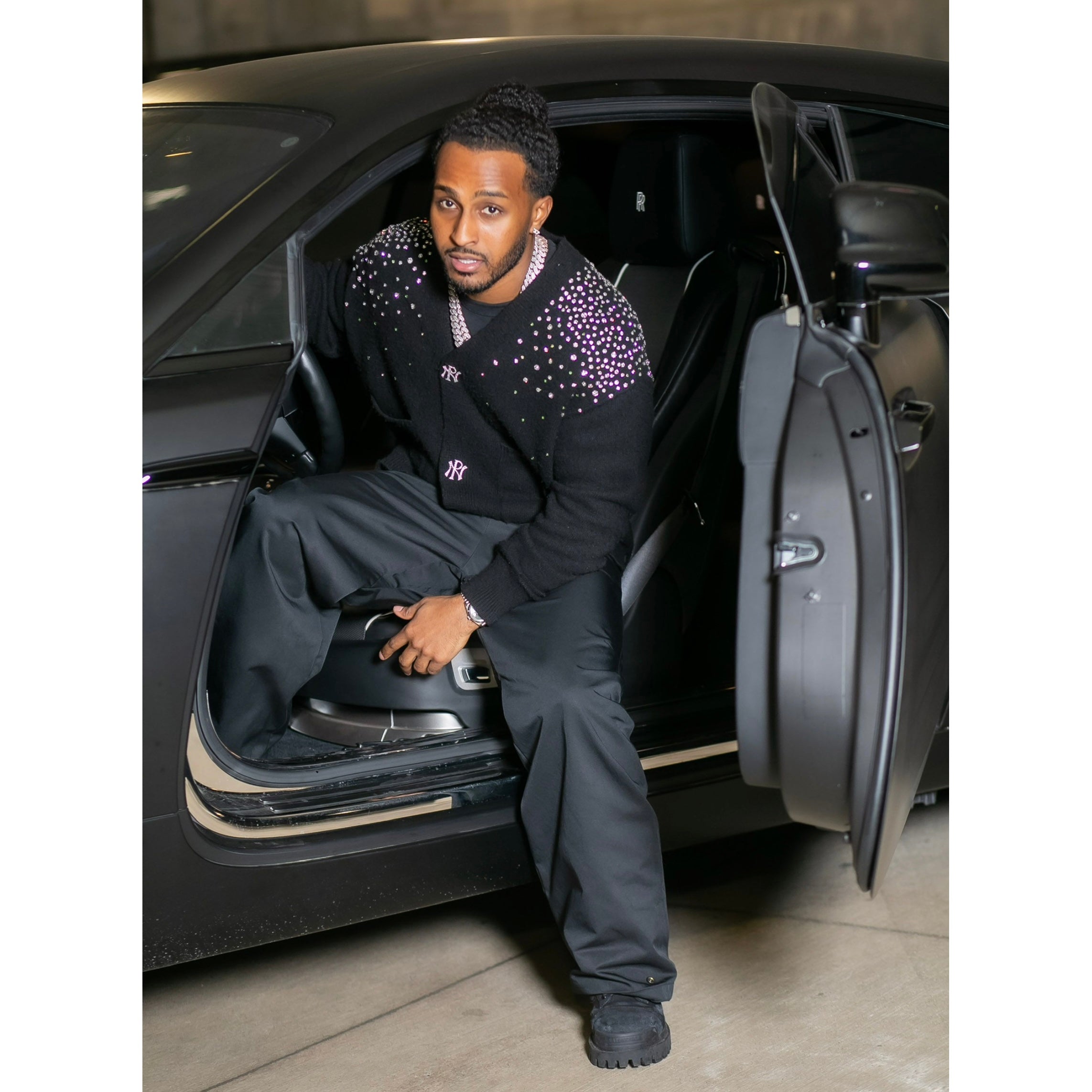 Man sitting in an open car door wearing a black outfit with purple accents.